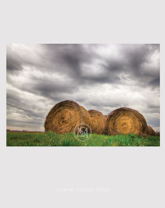 Neatly stacked hay bundles in a quiet  pasture beneath soft gray storm clouds, captured in limited edition Southern fine art photography.